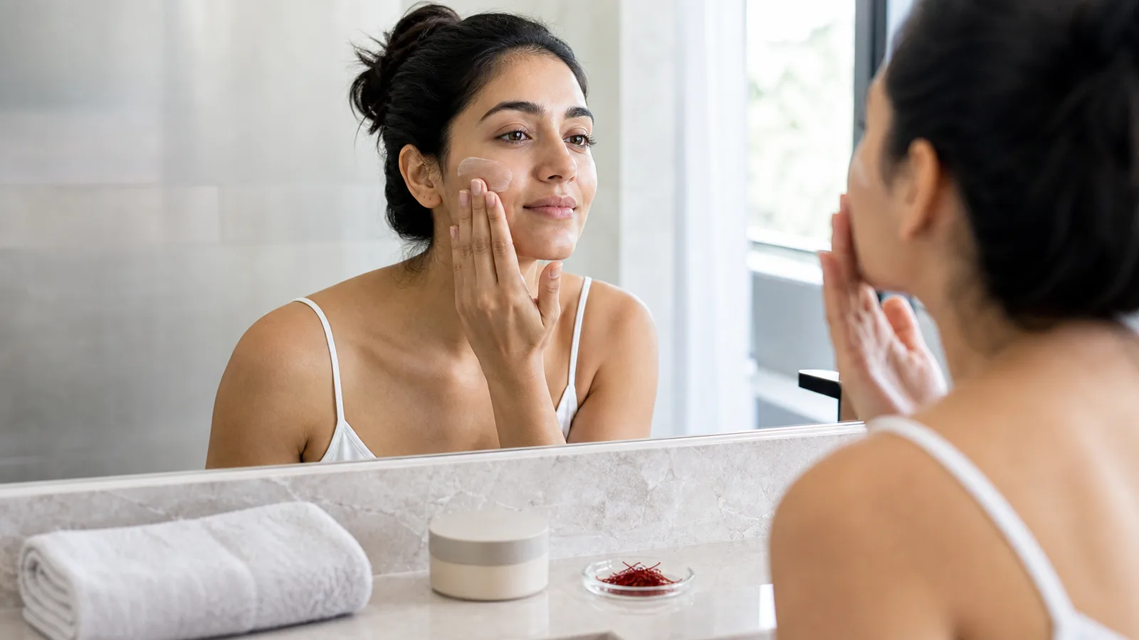 Woman applying moisturizer beside a small dish of saffron threads