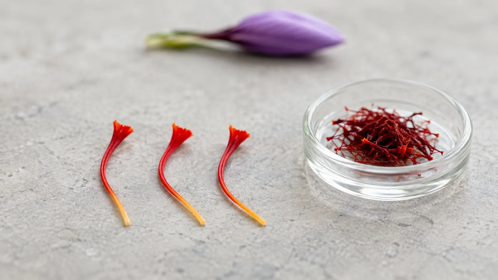 Three red saffron stigmas beside a dish of dried saffron threads